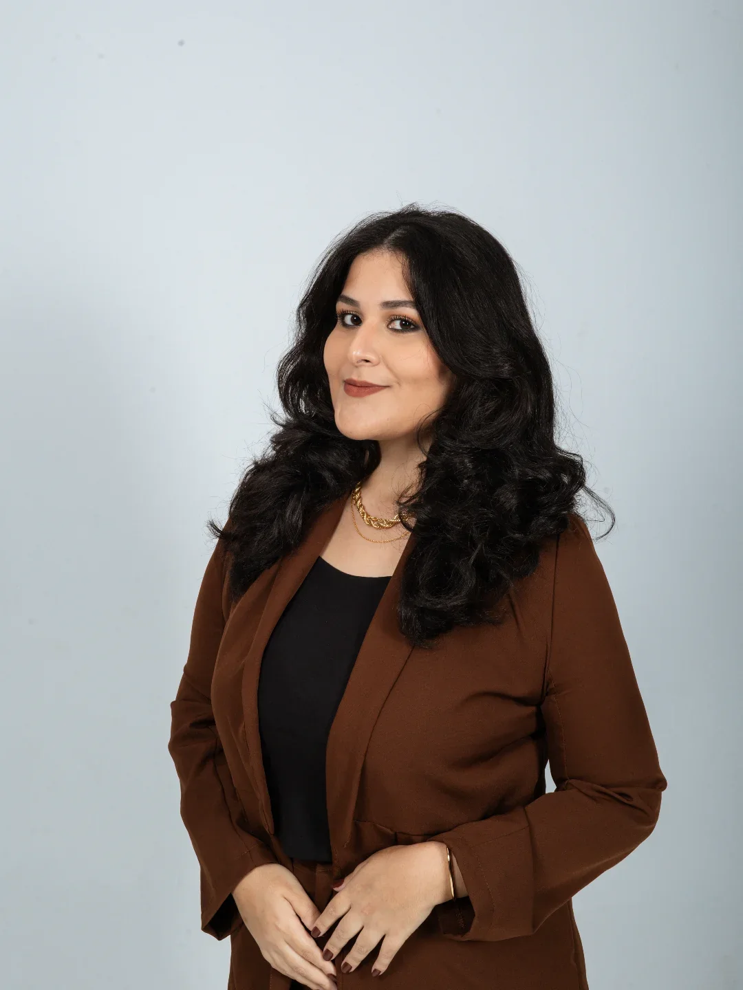 Dra. Linda Inês Alves, advogada, de blazer marrom e cabelo preto ondulado, olhando de lado com um leve sorriso.